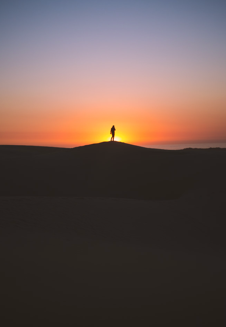 person standing on a hill with the sunset behind them